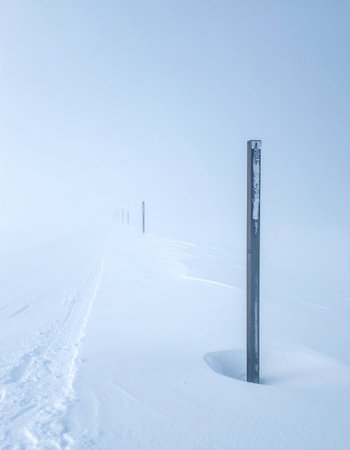 A solitary trail marker stands as a silent guide in a vast, minimalist winter landscape.の素材