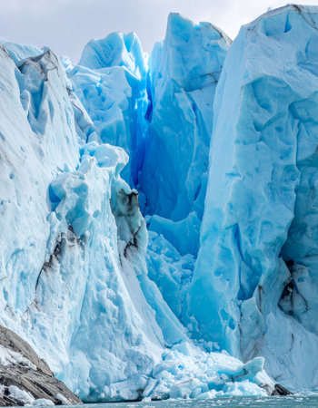 A close-up view reveals the immense power and ancient history of a towering glacier. Deep, vibrant blue hues glow from within the crevasses, showcasing the compressed ice formed over millennia.の素材
