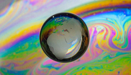 A macro photograph captures the delicate beauty of our planet, reflected as a fragile sphere floating on a sea of vibrant, chaotic colors.の素材