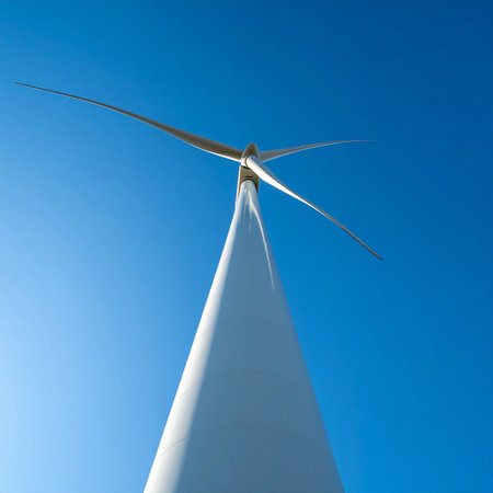 From a powerful low angle perspective, a sleek white wind turbine reaches towards a flawless, clear blue sky.の素材