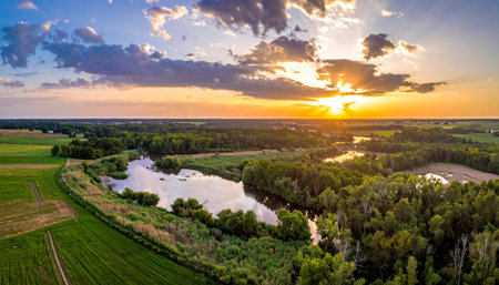 As the sun dips below the horizon, its golden rays cast a warm glow over a tranquil river valley.の素材