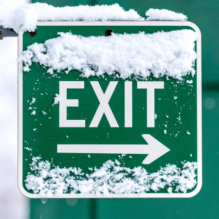 A green exit sign, partially obscured by a fresh blanket of snow, points the way forward.の素材