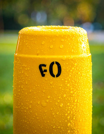 Morning dew collects on the vibrant yellow surface of a utility marker post, its stenciled 'FO' letters hinting at the infrastructure below.の素材