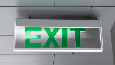 A brightly illuminated green exit sign glows against a modern, tiled wall, offering a clear path to safety.の素材