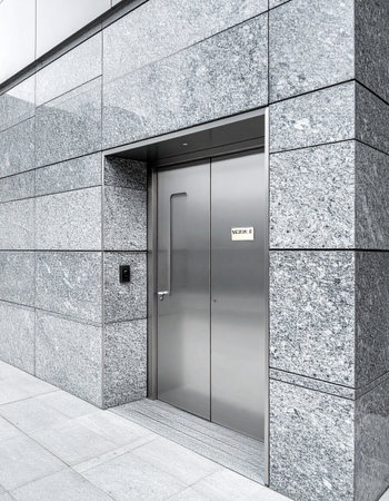 The closed, sleek stainless steel elevator door set against a polished granite wall suggests a modern and exclusive corporate environment.の素材