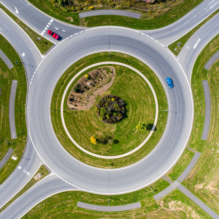 An aerial top-down perspective captures the seamless flow of traffic through a modern, circular roundabout.の素材