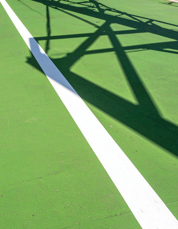 On a bright summer day, a sharp shadow falls across the vibrant green tennis court, intersecting the crisp white boundary line.の素材