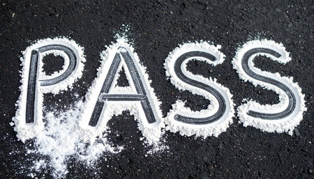 The word PASS is spelled out in a white granular powder on a dark asphalt surface, with the letters stylized to look like a road.の素材