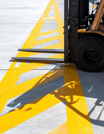 A forklift rests on a concrete surface, its forks perfectly aligned with bright yellow safety markings.の素材