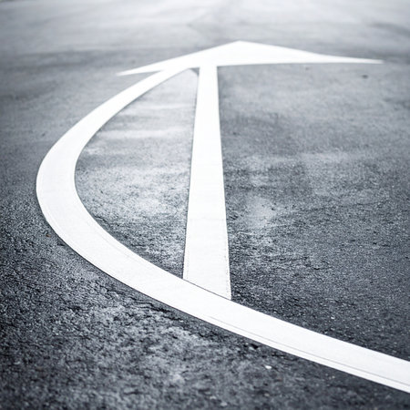 A single white arrow painted on rough, dark asphalt provides clear direction. A minimalist, high-contrast symbol of progress, guidance, and moving forward on a chosen path with purpose.の素材