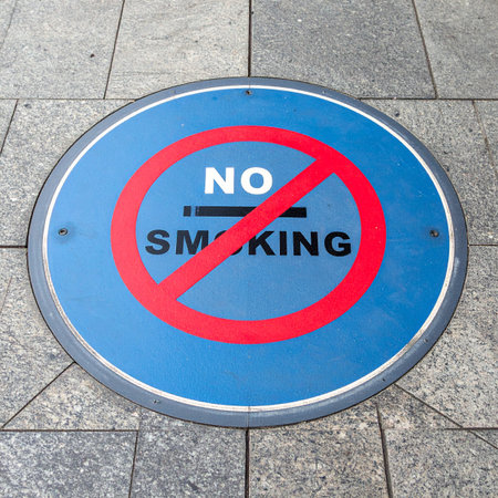 A bold 'No Smoking' sign is embedded in the urban pavement, a clear and direct message promoting public health and clean air.の素材