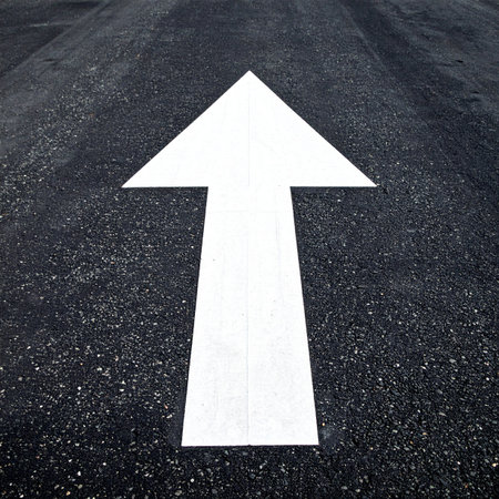 A crisp white arrow painted on dark, textured asphalt points the way forward.の素材