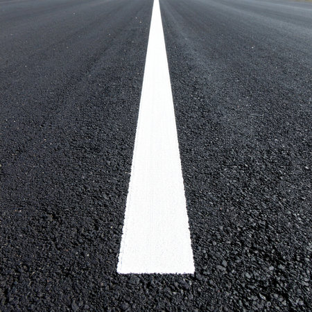 A crisp white line cuts a direct path forward on a dark, textured asphalt surface.の素材