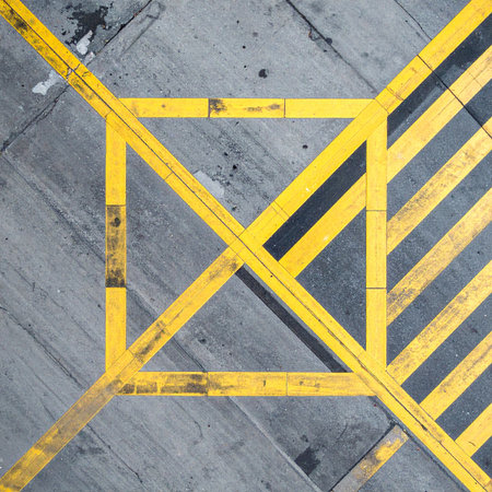 A high-angle, top-down view captures the stark geometry of yellow safety lines on a weathered gray concrete floor.の素材