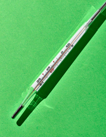 A vintage glass thermometer for measuring body temperature rests on a vibrant green background.の素材