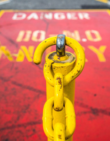 A bright yellow chain post stands as a stark sentinel against a vibrant red background stenciled with a clear warning.の素材
