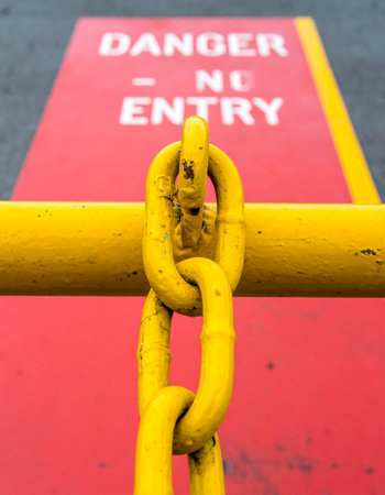 A heavy yellow chain hangs in front of a bold red 'Danger - No Entry' sign painted on the ground. The shallow focus emphasizes the barrier, creating a sense of immediate warning and restricted access.の素材