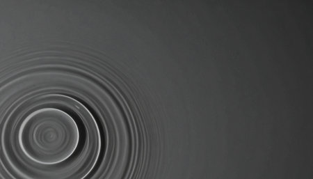 A single drop creates a series of perfect, concentric ripples expanding across a calm, dark water surface.の素材