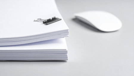 A minimalist workspace featuring a neat stack of documents and a computer mouse.の素材