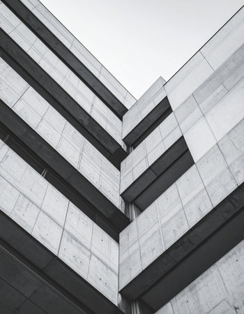 A low-angle, black and white view captures the imposing and severe lines of a modern concrete facade.の素材