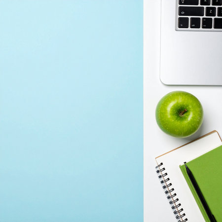 A clean and modern workspace captured from above. A fresh green apple sits beside a laptop and notebook, symbolizing a healthy balance between work, technology, and wellness.の素材