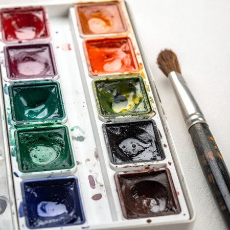 A well-loved watercolor palette, with colors mixed and ready, sits beside a paintbrush poised for the next stroke.の素材