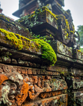 Vibrant green moss clings to the ancient, intricately carved stone walls of a sacred Balinese temple.の素材