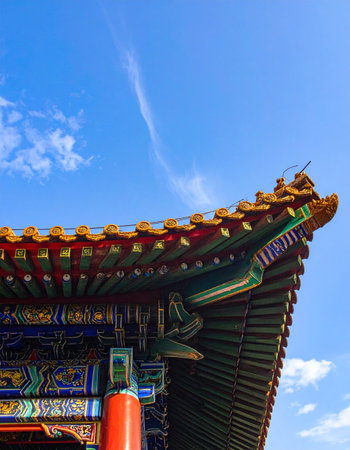 Looking up at the corner of a historic Chinese temple, the vibrant, ornate eaves stand out against a vast blue sky.の素材