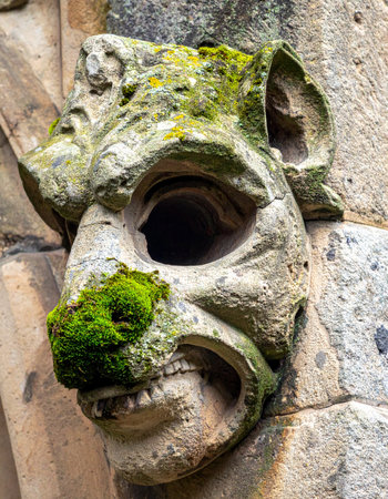 A close-up view of a weathered stone gargoyle, its ancient features now home to vibrant green moss.の素材