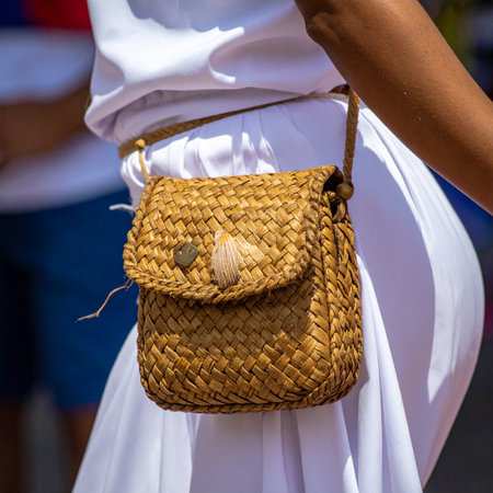A woman enjoys a sunny day out, her simple white dress perfectly complemented by a handmade woven straw bag.の素材