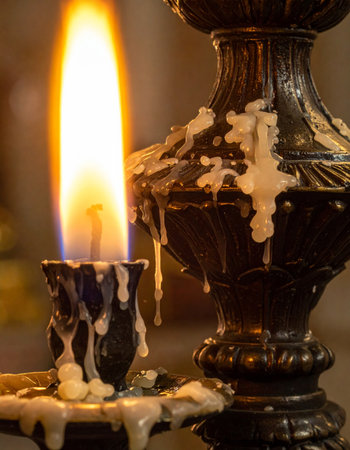 A single flame flickers atop a vintage candlestick, casting a warm, intimate glow in the darkness.の素材