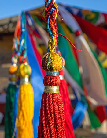 A vibrant red tassel, intricately woven with multi-colored threads, hangs in the foreground.の素材