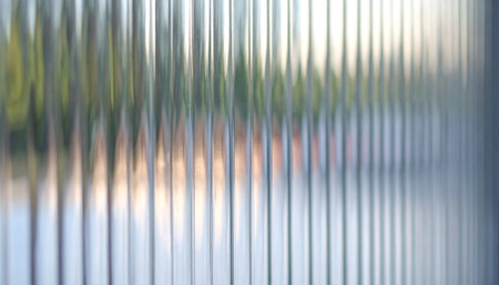 A serene, blurry landscape is viewed through a pane of fluted glass, distorting the natural colors into a soft, abstract pattern of vertical lines.の素材