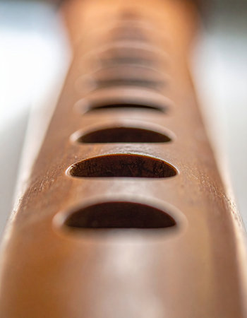 A macro perspective captures the repeating curved slits in a piece of warm, polished wood.の素材