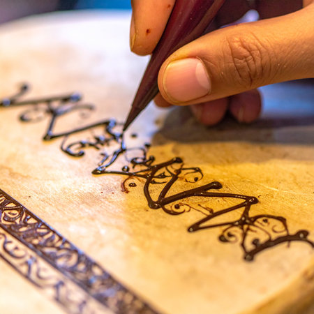With a steady hand, an artist carefully applies a traditional henna paste, squeezing the cone to create intricate swirls and patterns.の素材