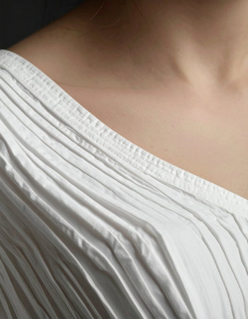A quiet moment captured in the elegant lines of a pleated white blouse. The soft fabric drapes gracefully over the shoulder, creating a study in texture, form, and minimalist beauty.の素材