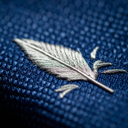A close-up macro shot reveals the exquisite detail of a silver feather emblem, meticulously embroidered onto a rich, textured navy blue fabric.の素材