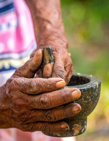 With hands weathered by time and experience, an elder carefully grinds herbs in a traditional stone mortar and pestle.の素材