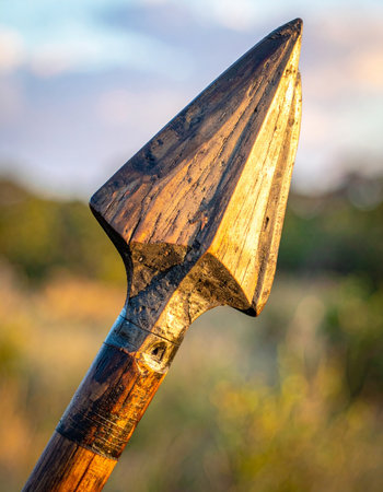A handcrafted wooden spearhead catches the last rays of the golden hour sun, its sharp point a testament to ancient survival skills and primitive hunting techniques.の素材