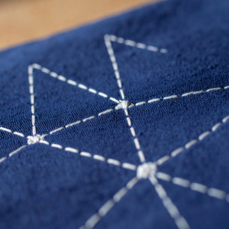 A close-up view of traditional Japanese sashiko embroidery, where white thread creates a geometric network pattern on deep indigo fabric.の素材
