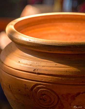 Warm, soft light catches the rich, earthy tones of a handcrafted clay pot.の素材