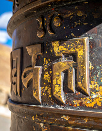 A close-up view reveals the sacred Tibetan script of the 'Om Mani Padme Hum' mantra on an ancient prayer wheel.の素材