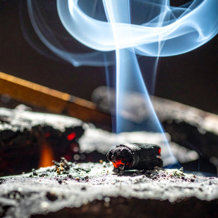 A glowing ember rests on a bed of soft ash, releasing a mesmerizing ribbon of blue smoke that dances and curls into the darkness.の素材