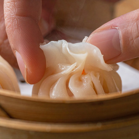 A close-up view captures the meticulous skill of a chef's hands as they expertly fold the delicate pleats of a traditional soup dumpling.の素材