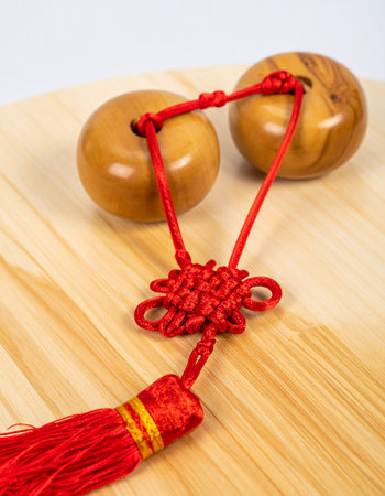 A vibrant red Chinese knot, a symbol of good luck and prosperity, rests on a natural wooden surface.の素材
