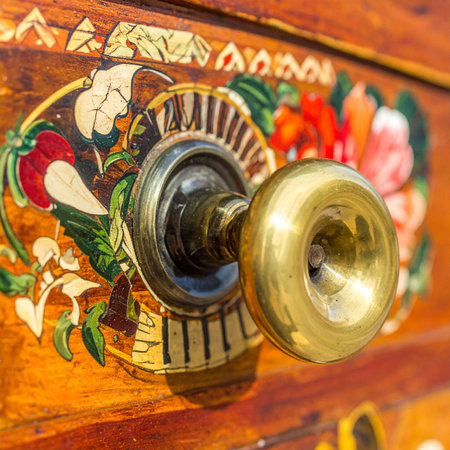 A close-up of an elegant, polished brass doorknob set against a backdrop of richly grained wood.の素材