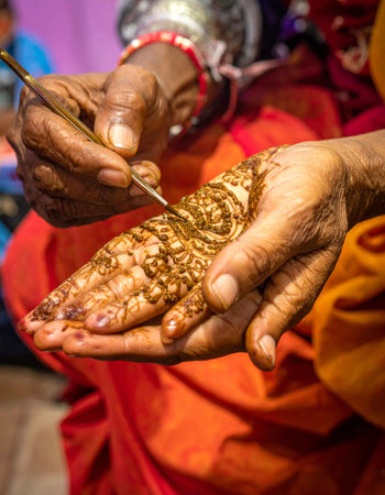 With a steady hand and a delicate tool, an artist carefully applies an intricate henna design onto a hand, a timeless ritual of beauty and celebration.の素材