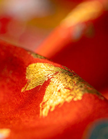 A close-up view reveals the intricate details of a luxurious red fabric, where threads of gold catch the light.の素材