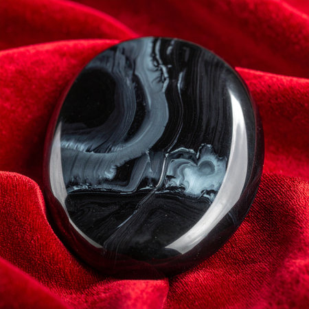 A polished, dark obsidian stone, known for its protective qualities, rests serenely on a bed of rich, luxurious red velvet.の素材