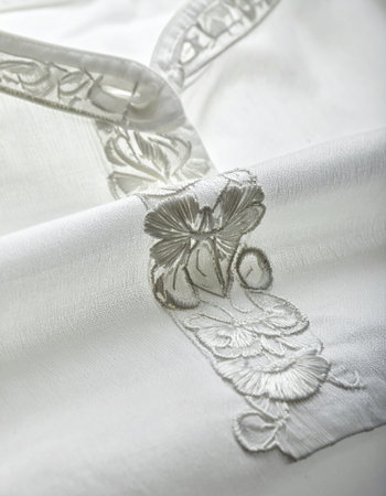 A close-up macro view reveals the meticulous detail of hand-stitched floral embroidery on a clean white fabric.の素材